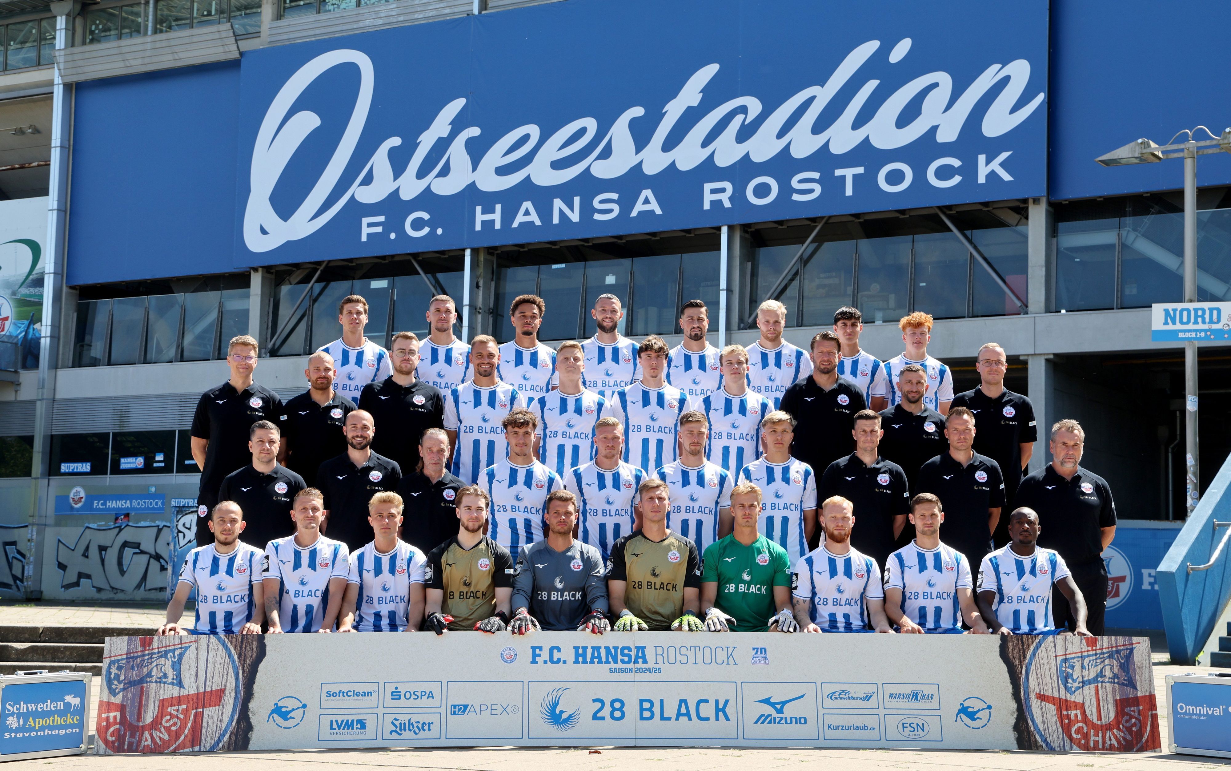 Die Mannschaftsmitglieder des Fußball-Drittligisten FC Hansa Rostock stehen bei einem Fototermin für ein Gruppenfoto nebeneinander vor dem Ostseestadion. Hauptsponsor „28 Black“ wirbt zwar weiter auf den Trikots, will die Partnerschaft mit dem Club aber vorzeitig beenden.
