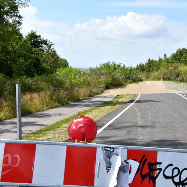 Eine rot-weiße Absperrbake, im Hintergrund ein Stück Straße, das an einem Weg endet.