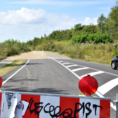 Eine rot-weiße Absperrbake, im Hintergrund ein Stück Straße, das an einem Weg endet.
