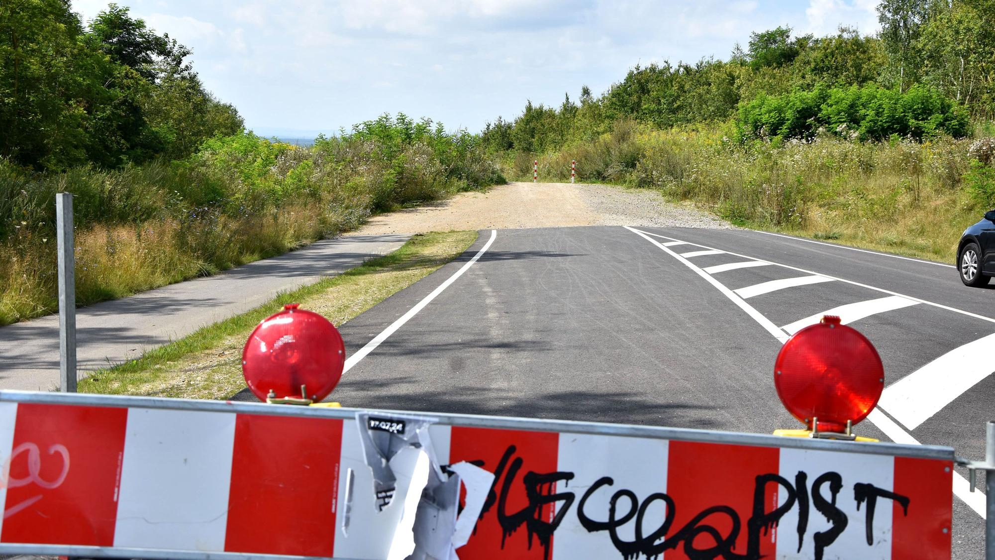 Eine rot-weiße Absperrbake, im Hintergrund ein Stück Straße, das an einem Weg endet.