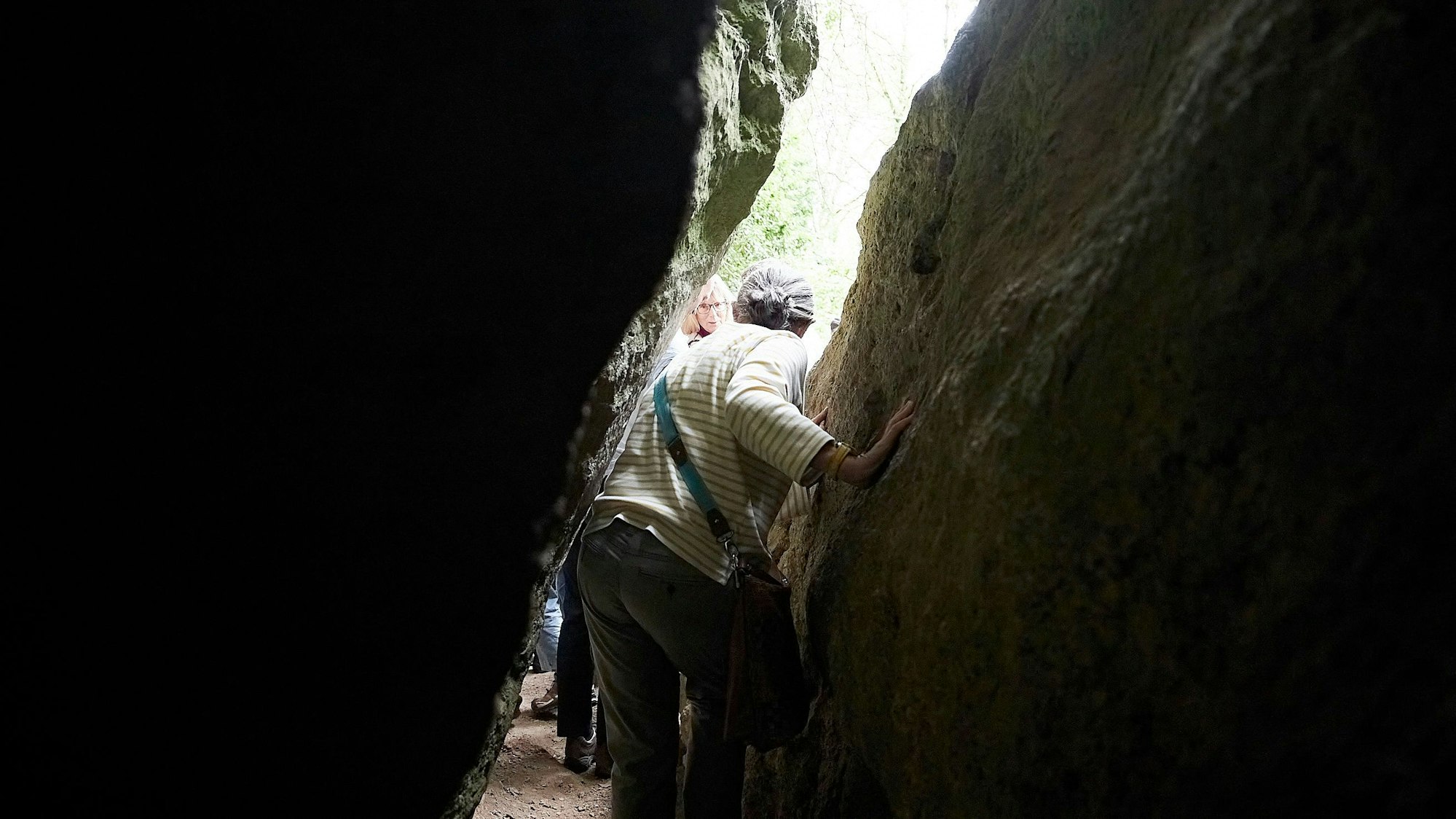 Eine Frau geht durch einen engen Spalt zwischen den Felsen der Kakushöhle bei Mechernich-Dreimühlen.