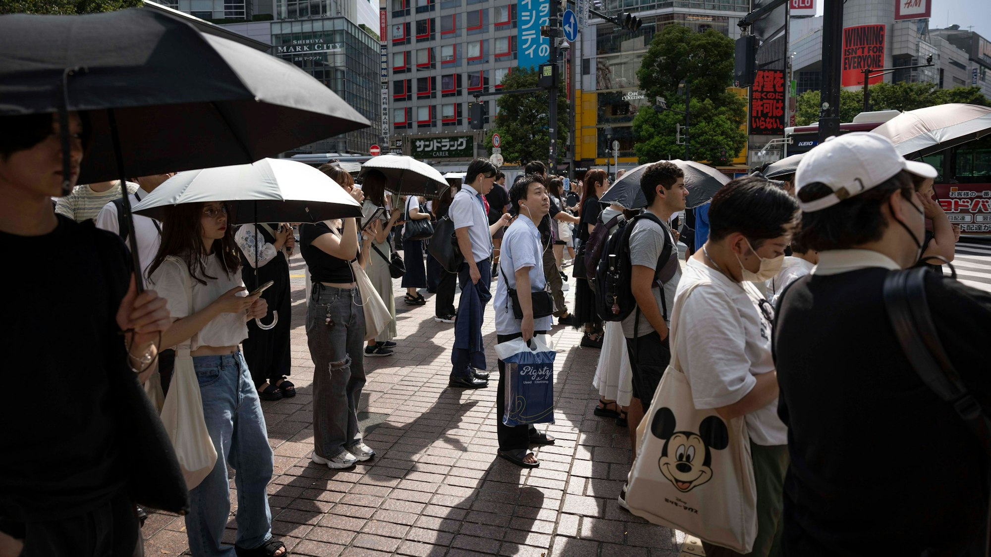Menschen stehen in Tokio mit Schirmen auf der Straße.