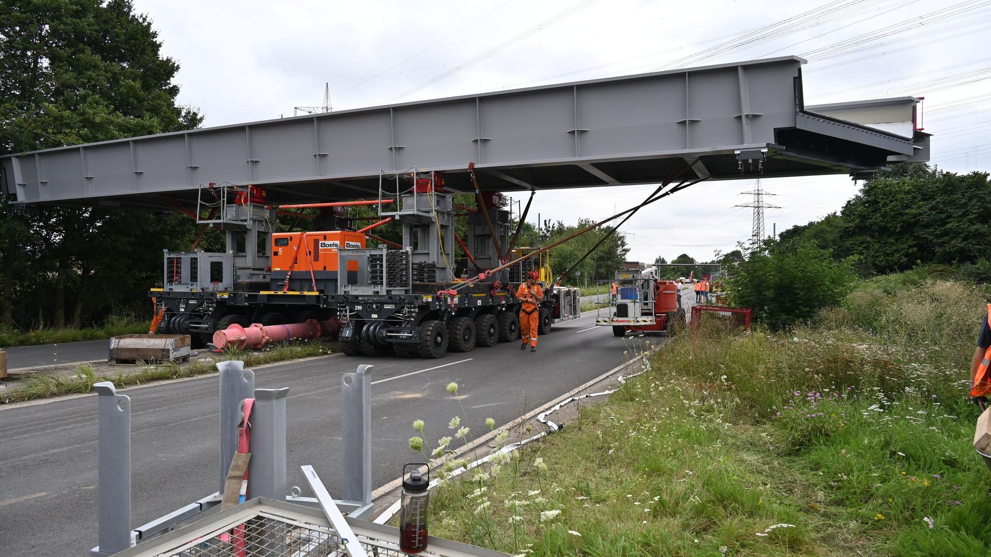Zwei Transportfahrzeuge schieben das Stahlbrückenteil quer über die Fahrbahn.