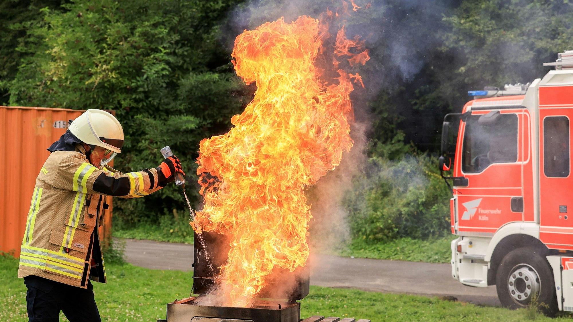 Ein Feuerwehrmann spritzt Wasser aus einer Flasche auf einen Fettbrand und erzeugt damit eine große Stichflamme.