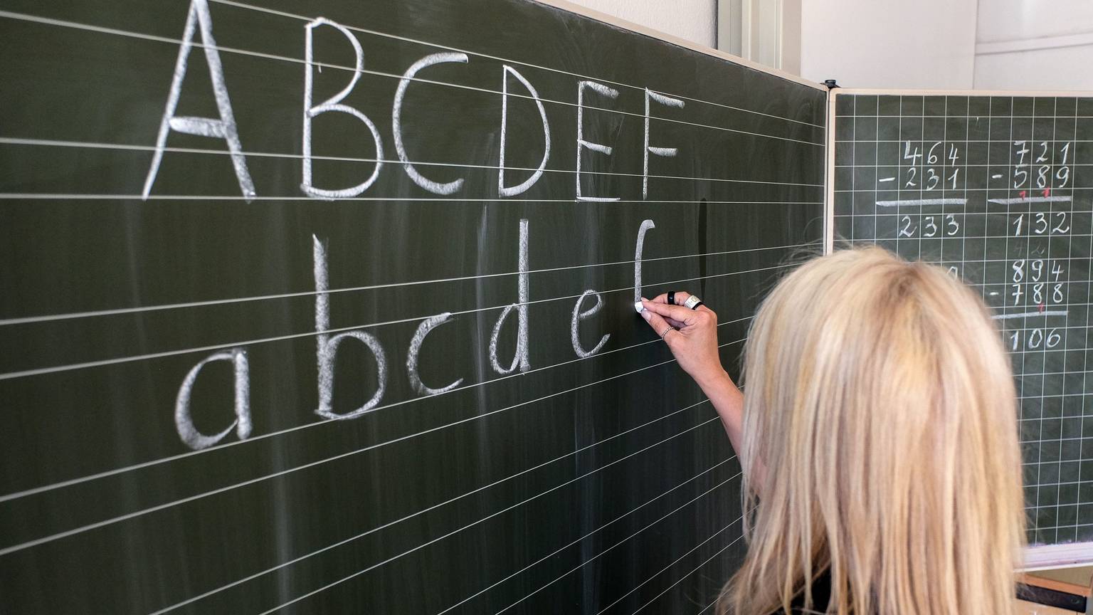 Eine Grundschullehrerin schreibt die ersten Buchstaben des Alphabets auf eine Schultafel in einem Klassenzimmer. (zu dpa: «Mehr als 90 Prozent der Lehrenden in Hamburg fest angestellt»)