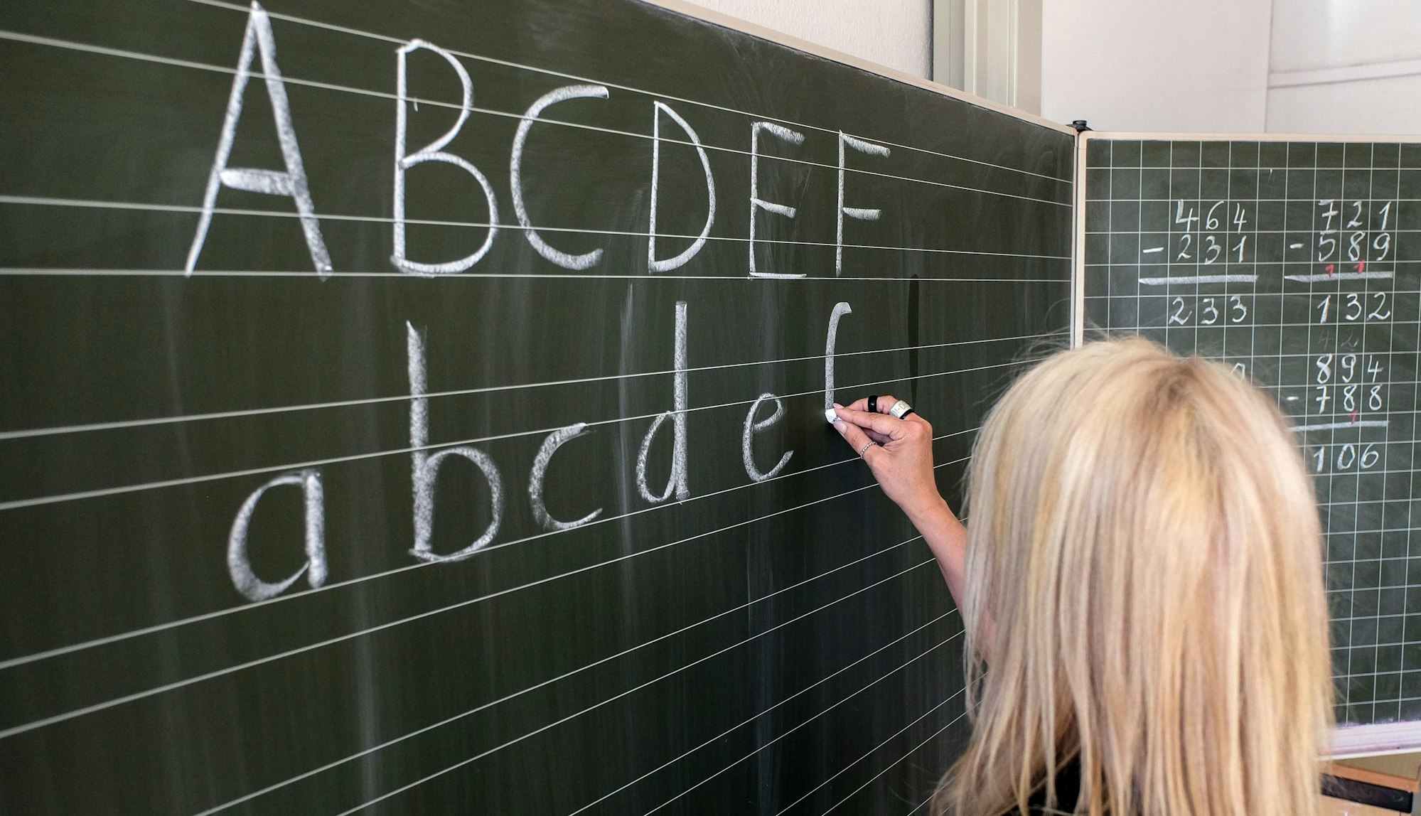Eine Grundschullehrerin schreibt die ersten Buchstaben des Alphabets auf eine Schultafel in einem Klassenzimmer. (zu dpa: «Mehr als 90 Prozent der Lehrenden in Hamburg fest angestellt»)