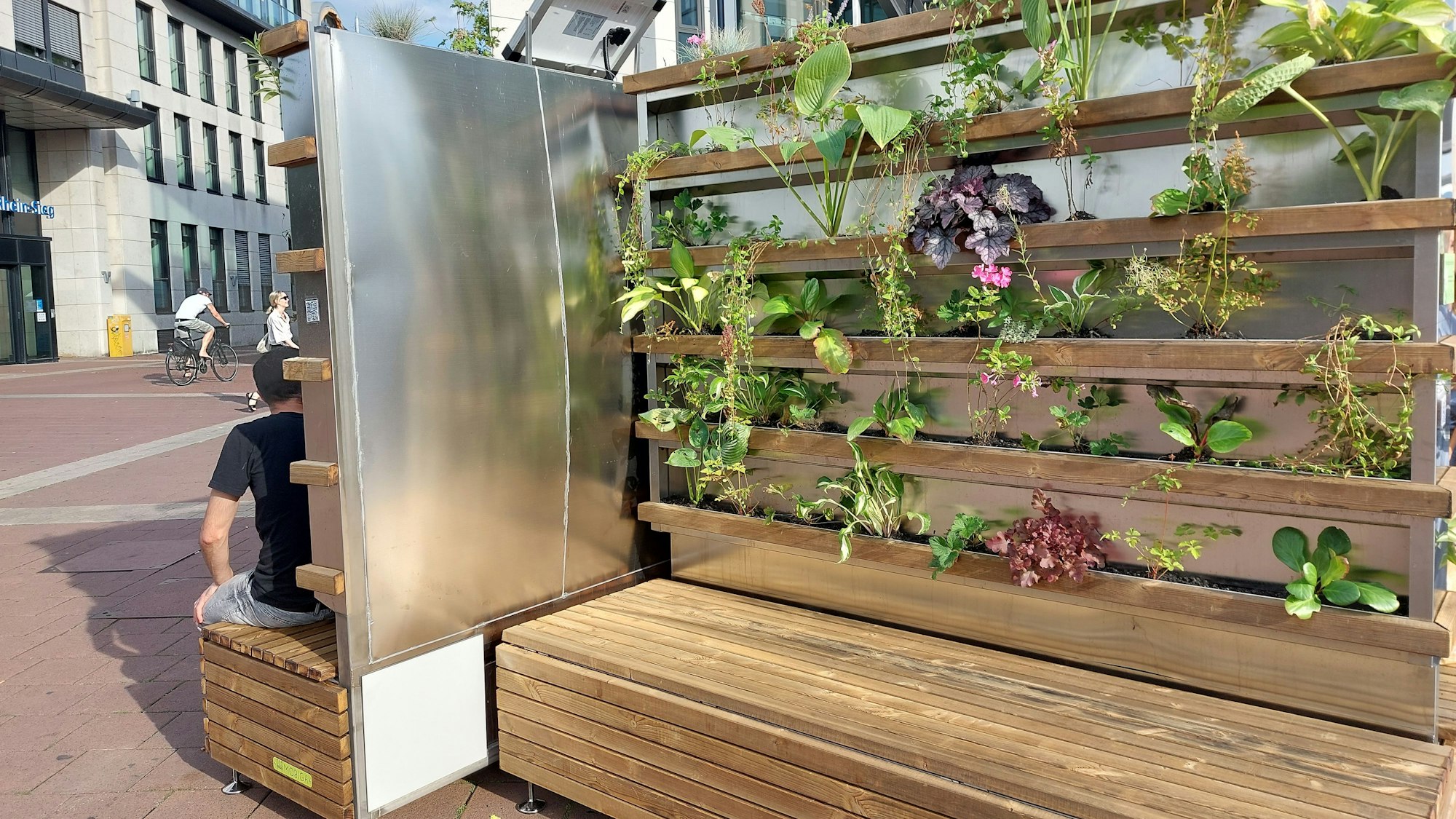 Hölzerne Sitzmöbel in einer Fußgängerzone. Die Rückwände sind bepflanzt.