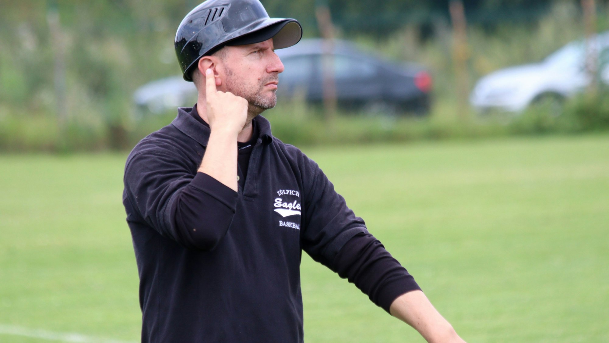 Der Zülpicher Base-Coach Chris Weis tippt sich mit dem Zeigefinger der rechten Hand gegen das Ohr. Er gibt so Anweisungen.