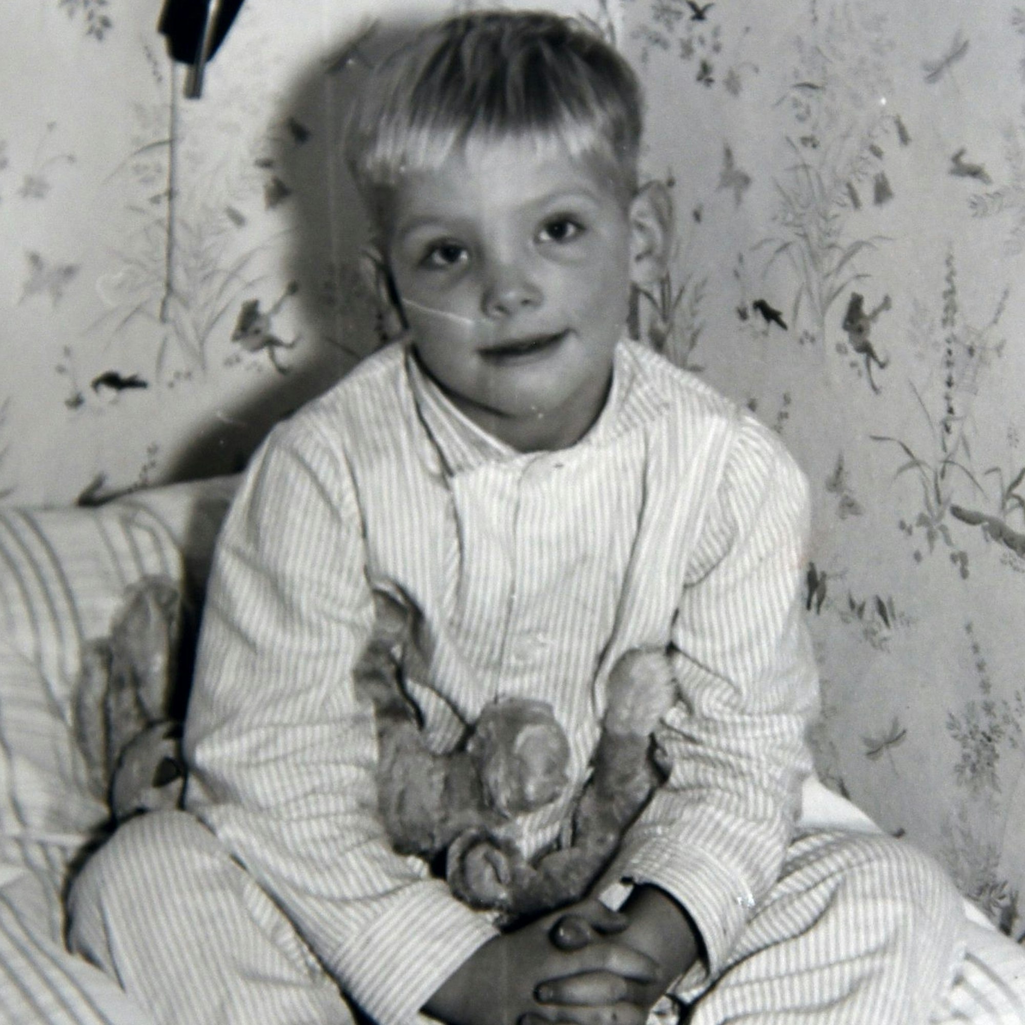 Ein kleiner Junge sitzt mit einem Plüschhasen auf dem Bett.