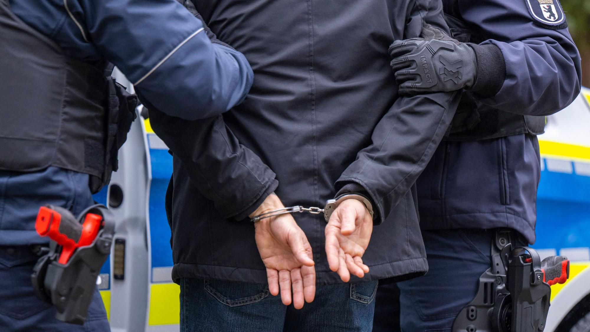 Zwei Polizeikräfte führen einen Mann in Handschellen ab.