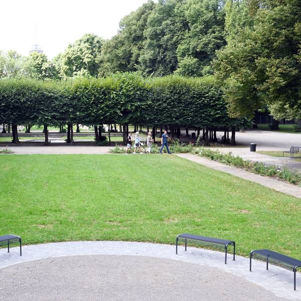 Zu sehen ist eine Grünfläche mit Sitzbänken, Kieswegen, Lindenbäumen und Blumenbeeten.