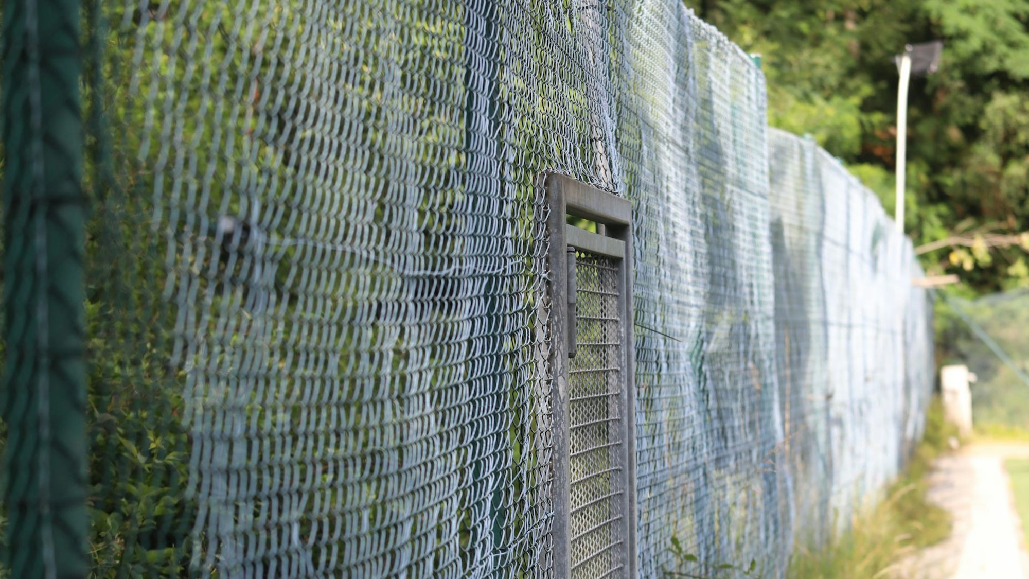 Ein stark lädierter und welliger Maschendrahtzaun.