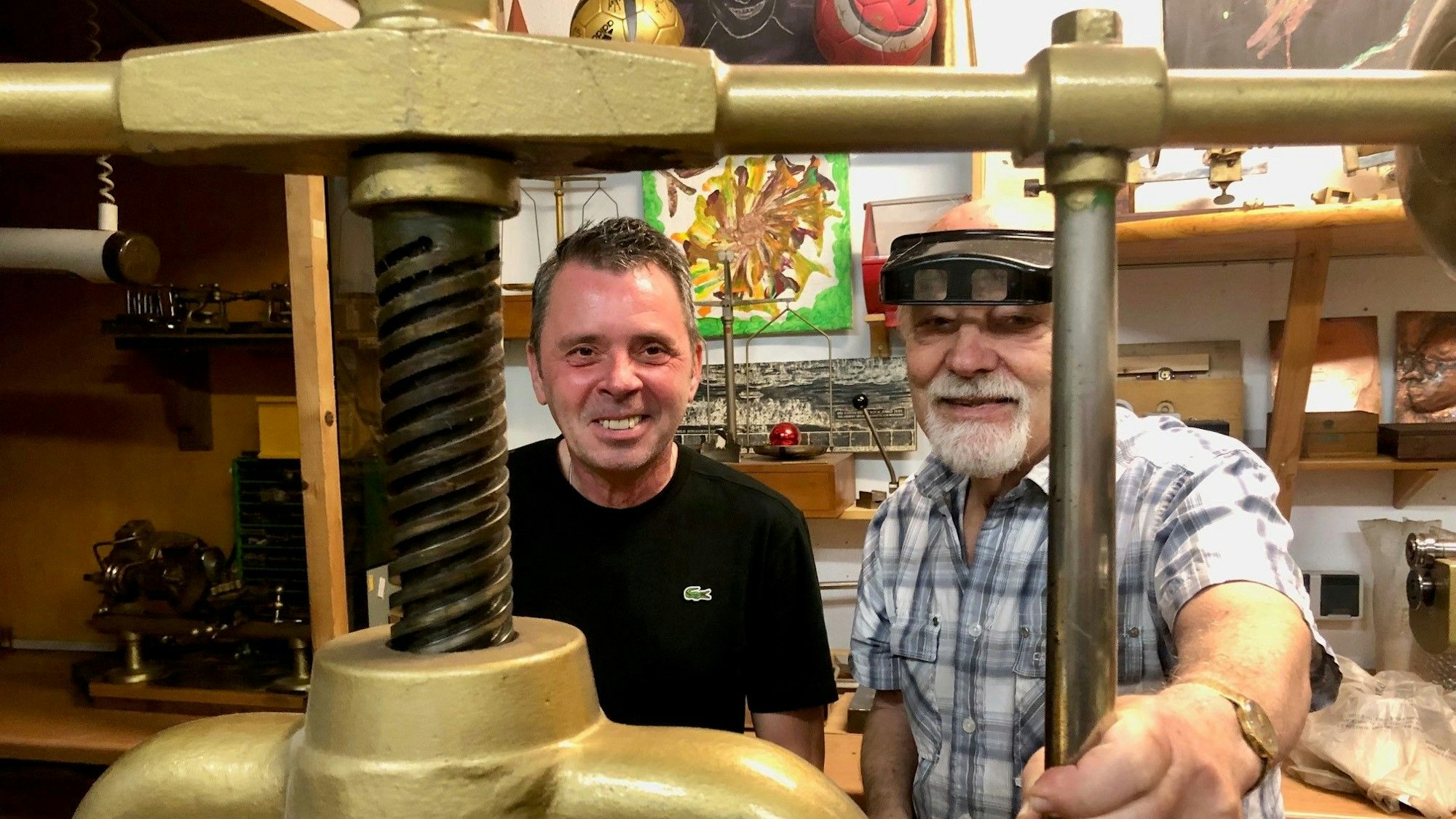 Friseurmeister Ralph Schwalbach (links) und Goldschmiedemeister Herbert Schmelzerstehen hinter einer antiken Schmuckpresse.