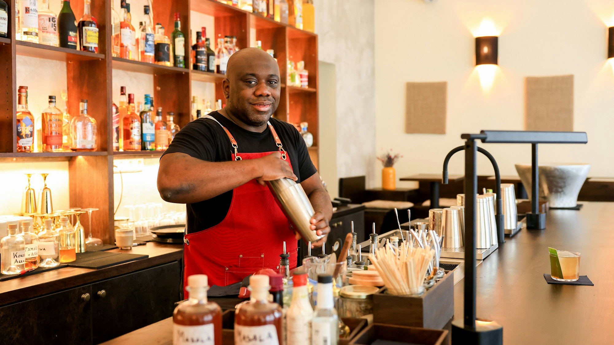 Barchef Samuél Antonio Bernardo steht an der Bar und hat einen Shaker in der Hand. Er lächelt in die Kamera.