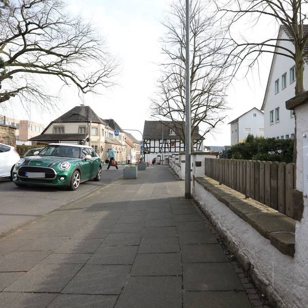 Ein grünes Auto auf einer Straße, im Hintergrund quert ein Fußgänger die Fahrbahn.