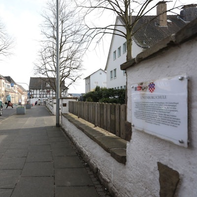 Ein grünes Auto auf einer Straße, im Hintergrund quert ein Fußgänger die Fahrbahn.