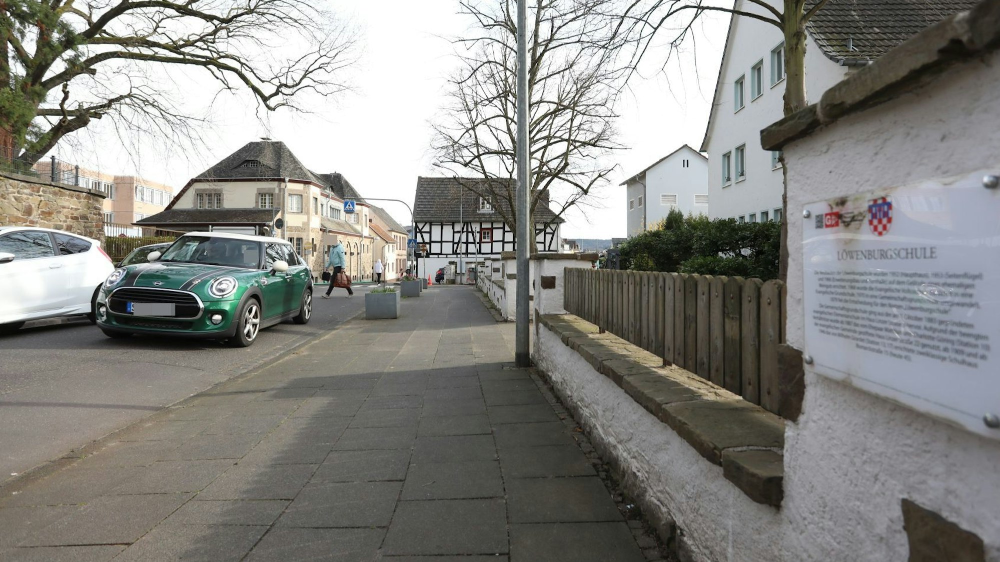 Ein grünes Auto auf einer Straße, im Hintergrund quert ein Fußgänger die Fahrbahn.