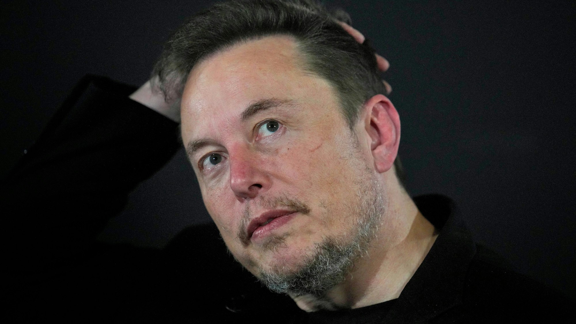 Elon Musk in Nahaufnahme: Er ist unrasiert, fährt sich mit der Hand durch die Haare.