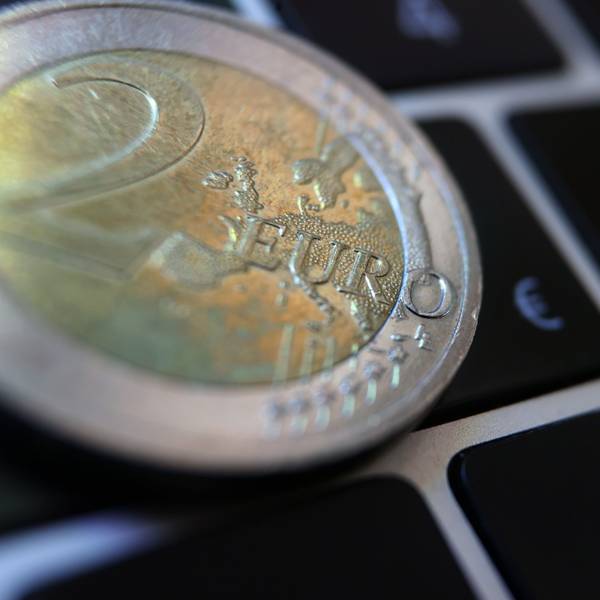 Eine Zwei-Euro-Münze liegt auf der Tastatur eines Laptops neben einem Eurozeichen (Symbolfoto).