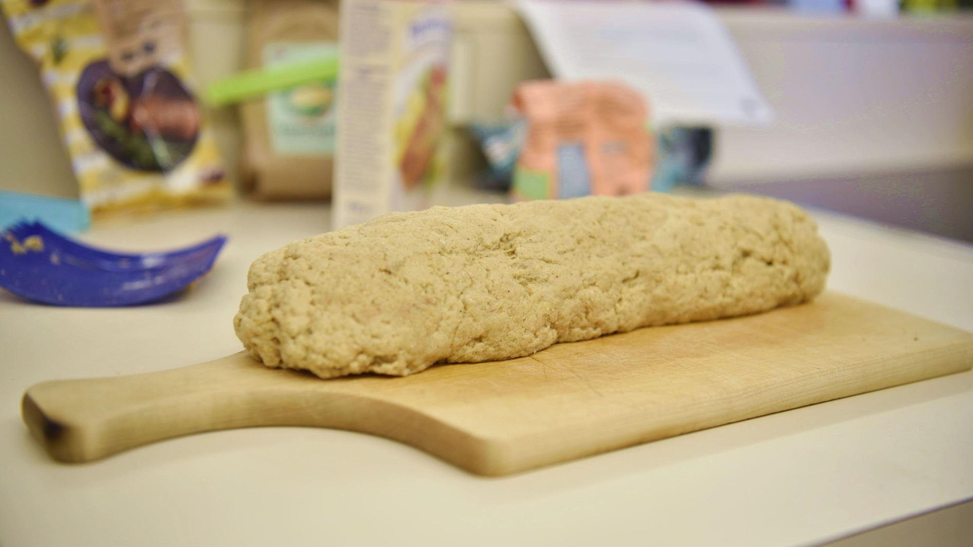 Ein Strang Seitan-Teig liegt auf einem Holzbrett auf einer Küchenarbeitsplatte.