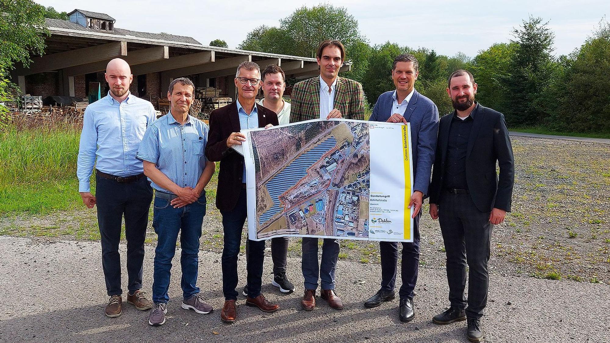 Eine Gruppe Männer steht auf dem Gelände des Sägewerks, einige halten einen Plan.