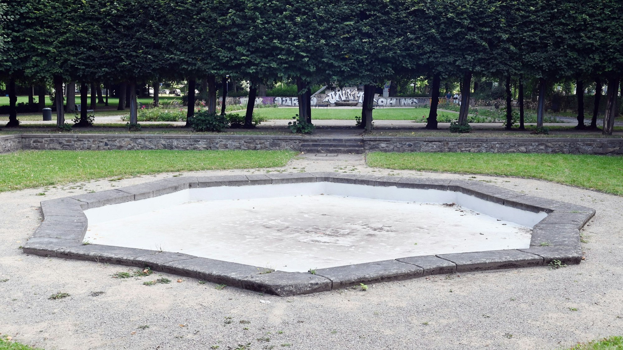 Zu sehen ist das trocken gelegte Becken eines Brunnens in der Grünanlage Alhambra in Nippes.