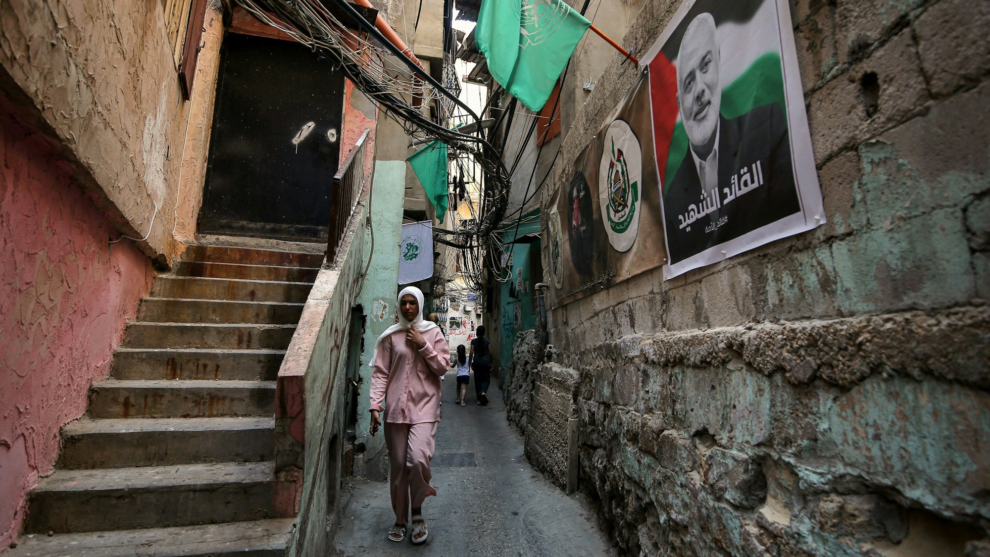 07.08.2024, Libanon, Beirut: Ein palästinensisches Mädchen geht an einem Plakat des ehemaligen Hamas-Führers Hanija in einer der engen Gassen des Beiruter Lagers Burj el-Barajneh vorbei. Knapp eine Woche nach der Tötung von Hamas-Auslandschef Ismail Hanija hat die islamistische Terrorgruppe Sinwar zum neuen Anführer der Organisation bestimmt. Das teilte die Hamas auf der Plattform Telegram mit. Foto: Marwan Naamani/dpa +++ dpa-Bildfunk +++