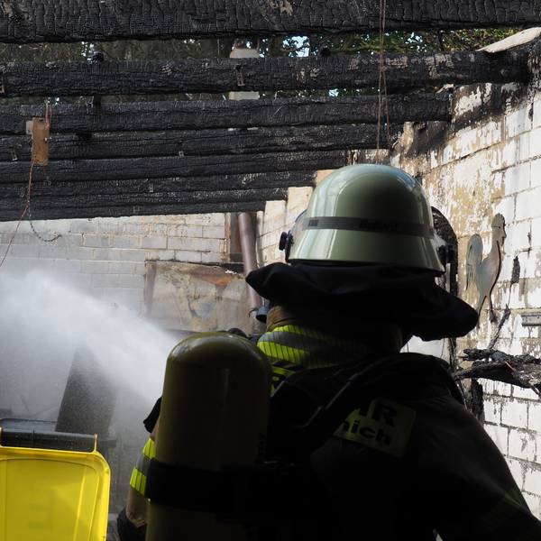 Mit einem Wasserstrahl kühlt ein Feuerwehrmann eine Flasche mit Acetylen bei einem Brand in Antweiler.