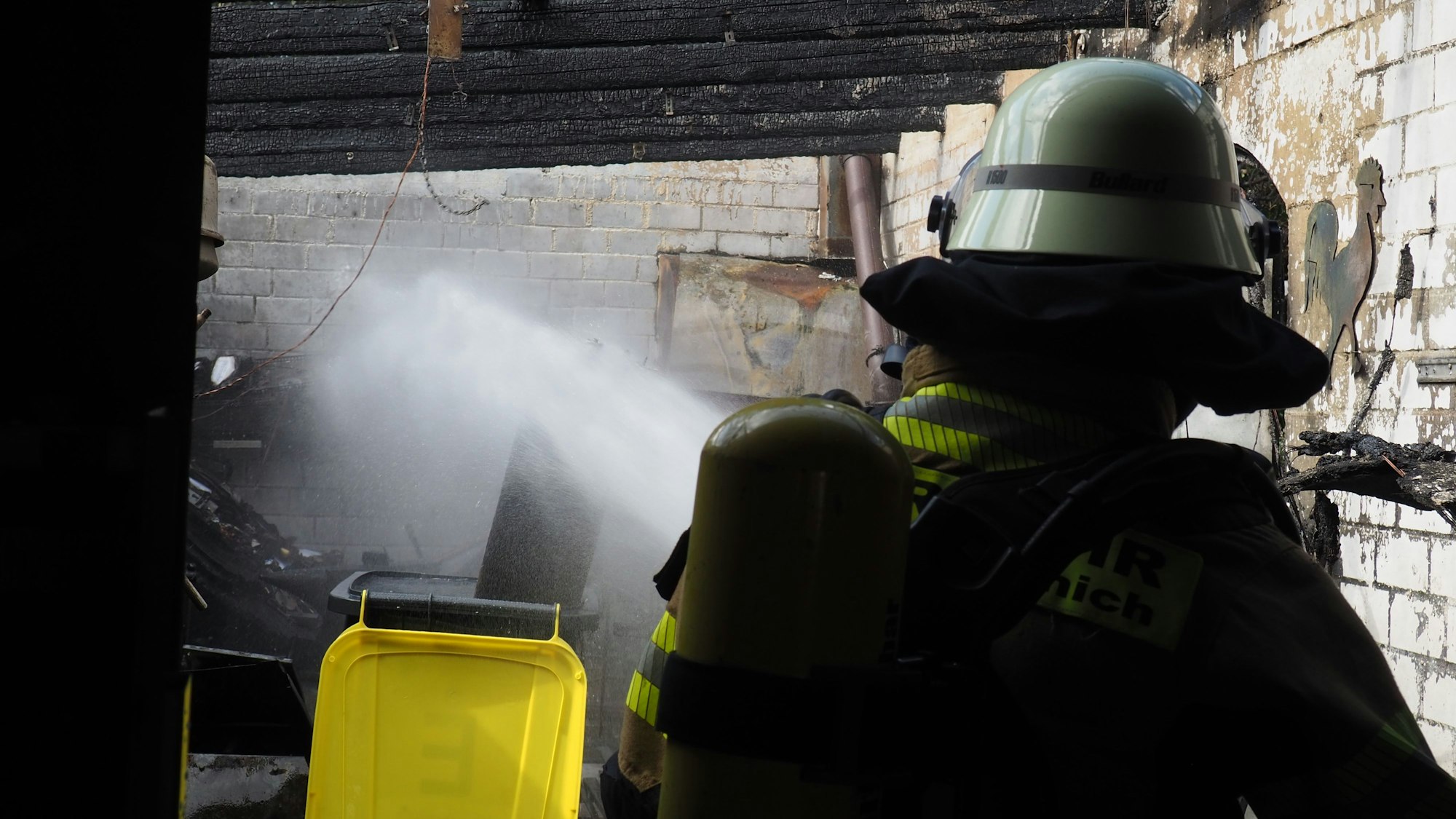 Mit einem Wasserstrahl kühlt ein Feuerwehrmann eine Flasche mit Acetylen bei einem Brand in Antweiler.