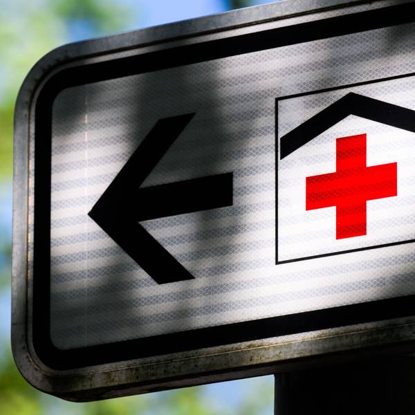 Ein Piktogramm mit einem roten Kreuz auf einem Straßenschild weist den Weg zu einem Krankenhaus.