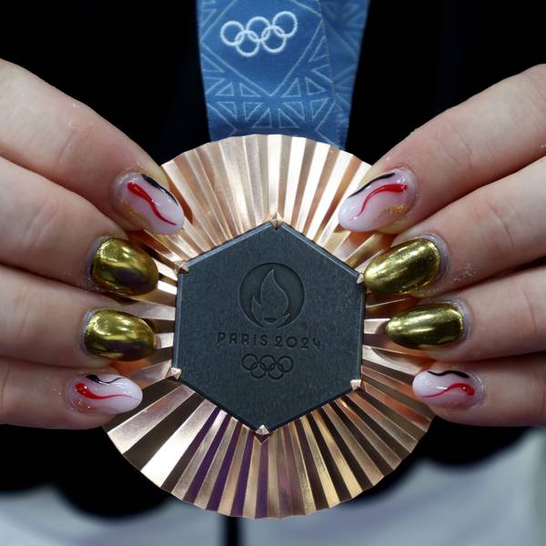 Die Hände einer Frau präsentieren eine olympische Bronzemedaille an blauem Band. Die Fingernägel der Dame sind in unterschiedlichen Farben, metallisch und rosa, rot, schwarz lackiert.