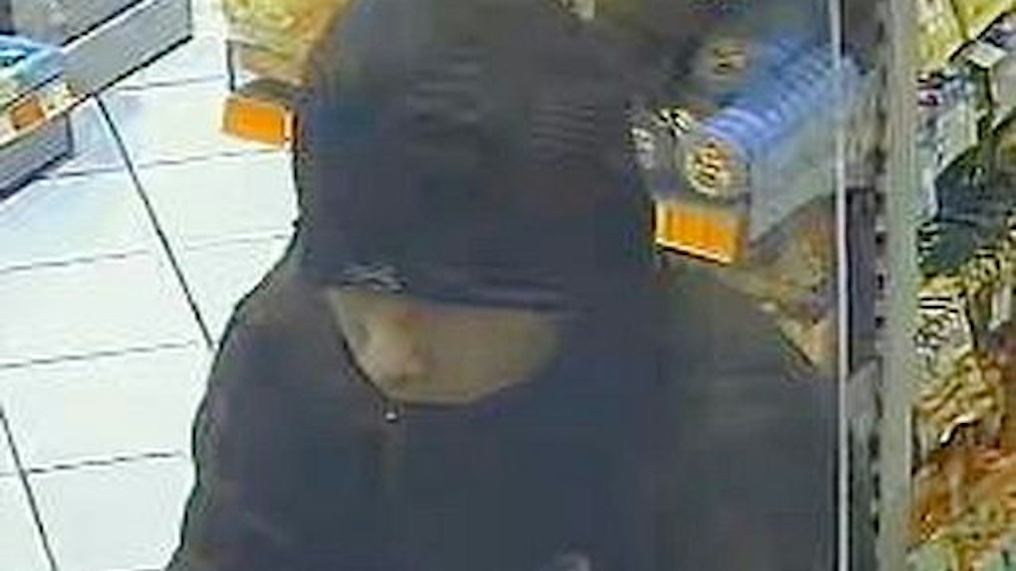 Das Bild zeigt einen vermummten Mann an der Kasse. Er überfällt eine Tankstelle.