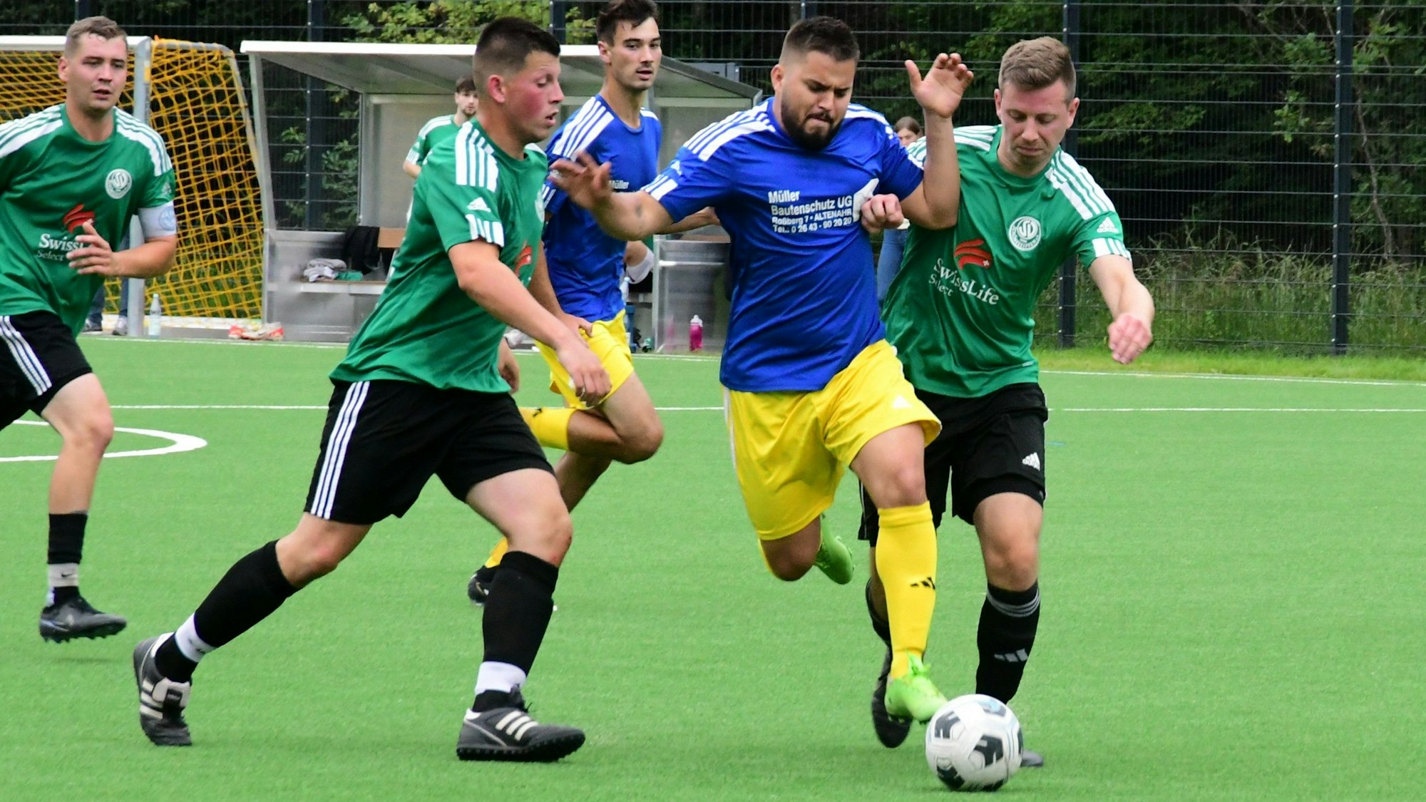 Ein Fußballspieler tankt sich mit Ball durch mehrere Gegenspieler. Dabei hat er beide Arme erhoben.