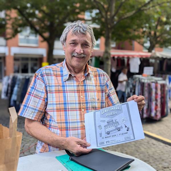 Marktmeister Hans-Josef Lang mit einem Entwurf für den Flyer zum Genussmarkt vor den Ständen des Wochenmarkts.