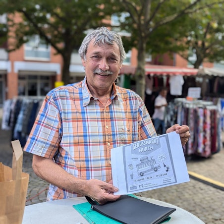 Marktmeister Hans-Josef Lang mit einem Entwurf für den Flyer zum Genussmarkt vor den Ständen des Wochenmarkts.