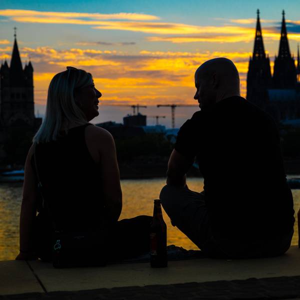 Das Bild zeigt zwei Personen im Sonnenuntergang. Im Hintergrund sieht man den Kölner Dom.