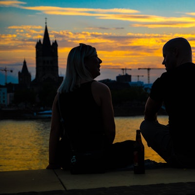 Das Bild zeigt zwei Personen im Sonnenuntergang. Im Hintergrund sieht man den Kölner Dom.