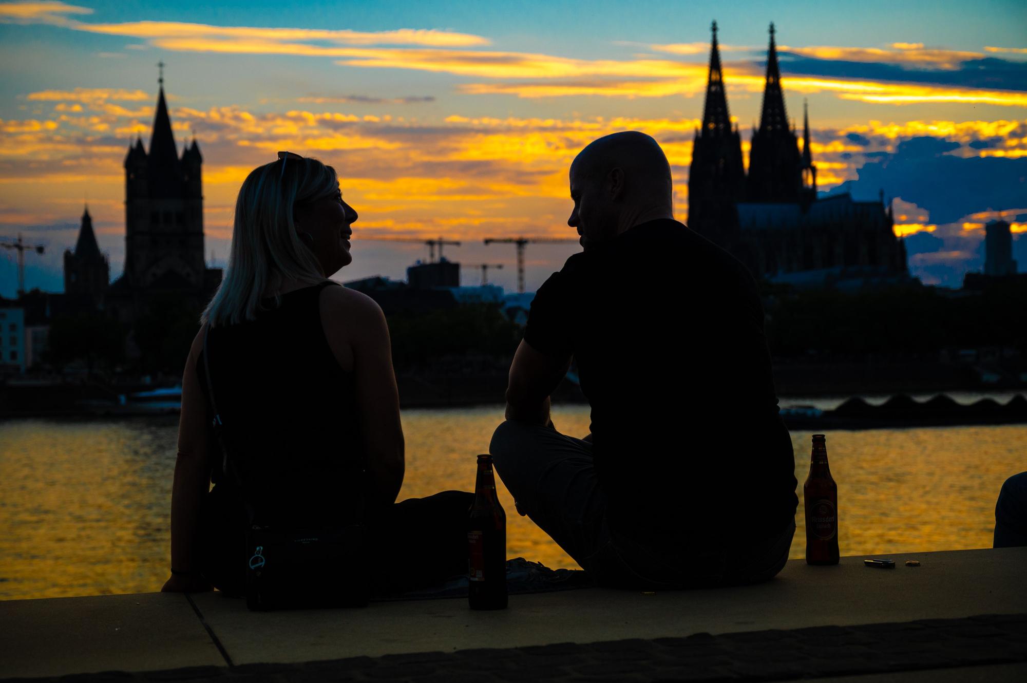 Das Bild zeigt zwei Personen im Sonnenuntergang. Im Hintergrund sieht man den Kölner Dom.