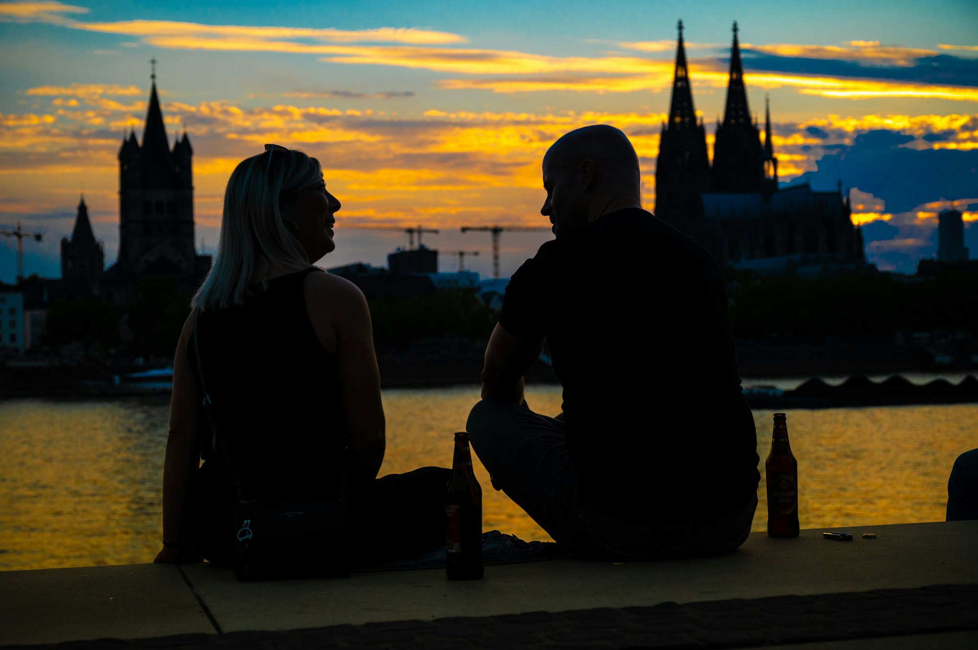 Das Bild zeigt zwei Personen im Sonnenuntergang. Im Hintergrund sieht man den Kölner Dom.