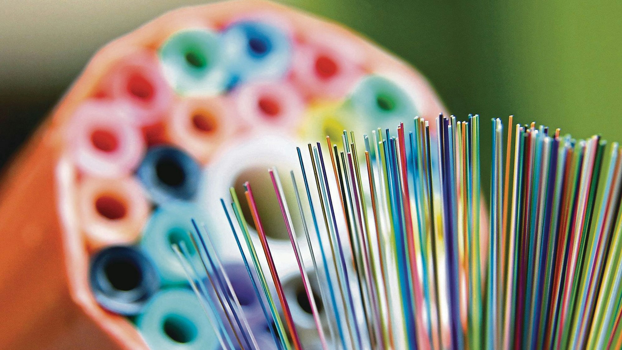 Eine Frau hält ein Kabelbündel aus Glasfaserkabeln vor einer sogenannten Speedpipe (Leerrohr) für ein Glasfasernetzwerk.