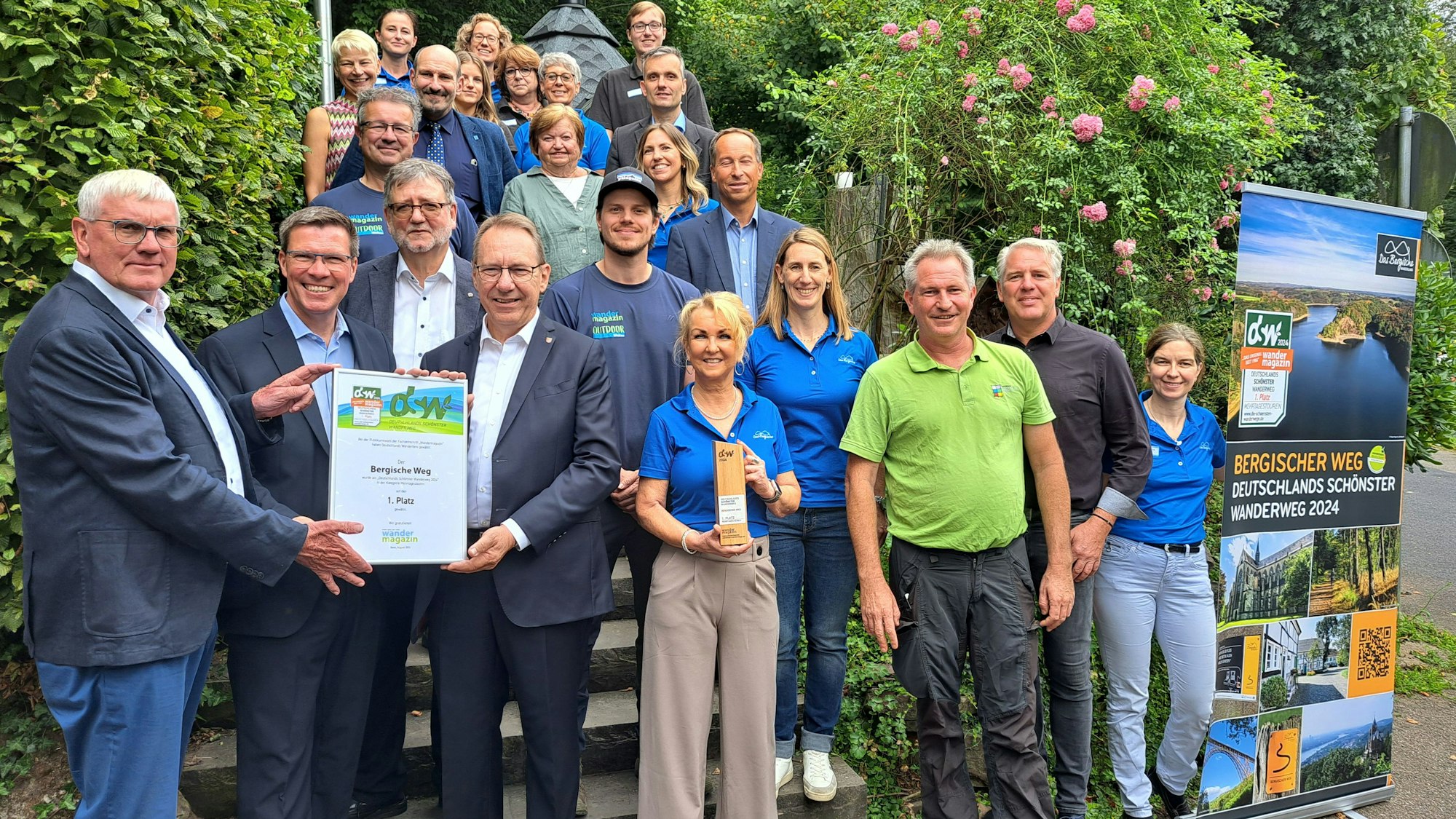Menschen stehen mit einer Urkunde und eine Trophäe für „Deutschlands schönsten Wanderweg“ auf einer Treppe am Hotel Restaurant Wißkirchen in Otdenthal-Altenberg.
