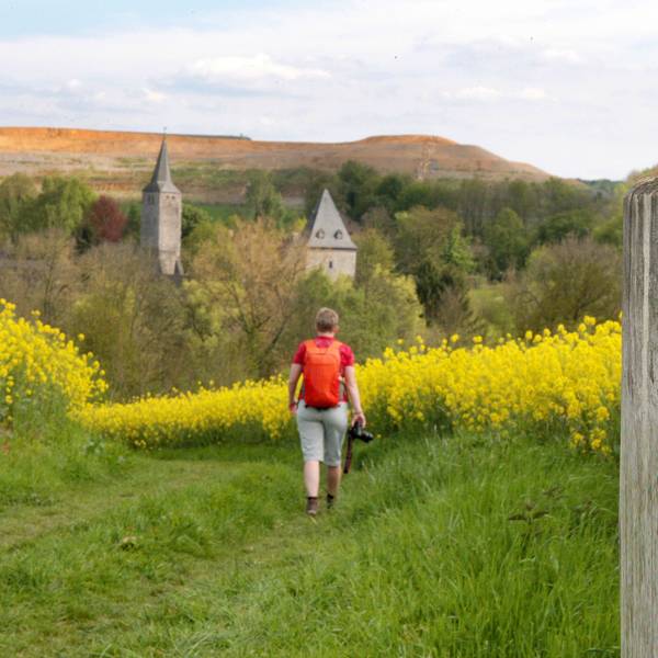 Eine Frau geht auf dem Bergischen Weg über eine Wiese.