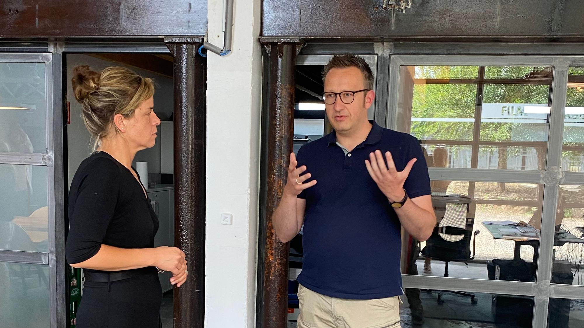 Mona Neubauer, NRW-Ministerin für Wirtschaft, Industrie, Klima und Energie, steht neben Philipp
Klietz und sieht ihn an. Der Inhaber der Filmproduktionsfirma AV22+, gestikuliert mit seinen Händen.