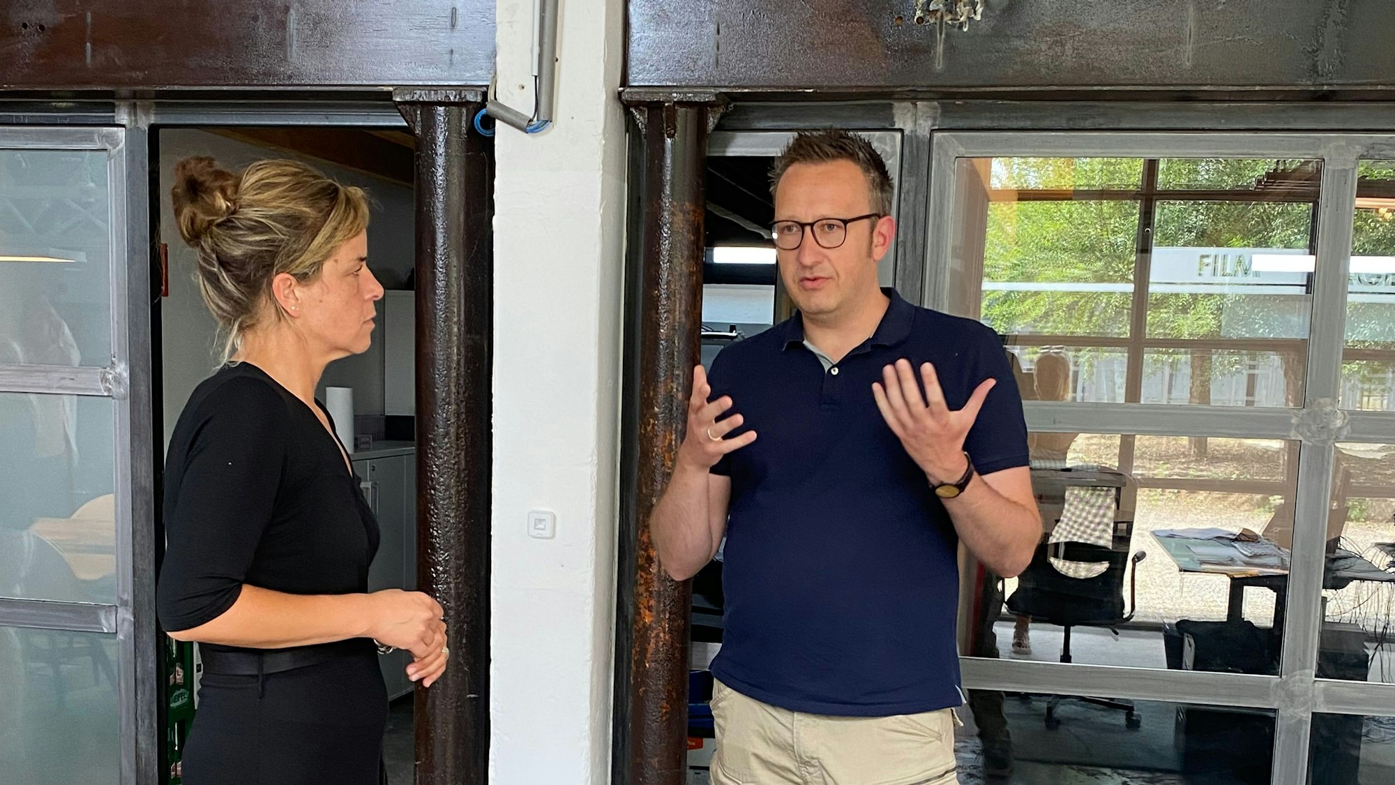 Mona Neubauer, NRW-Ministerin für Wirtschaft, Industrie, Klima und Energie, steht neben Philipp
Klietz und sieht ihn an. Der Inhaber der Filmproduktionsfirma AV22+, gestikuliert mit seinen Händen.