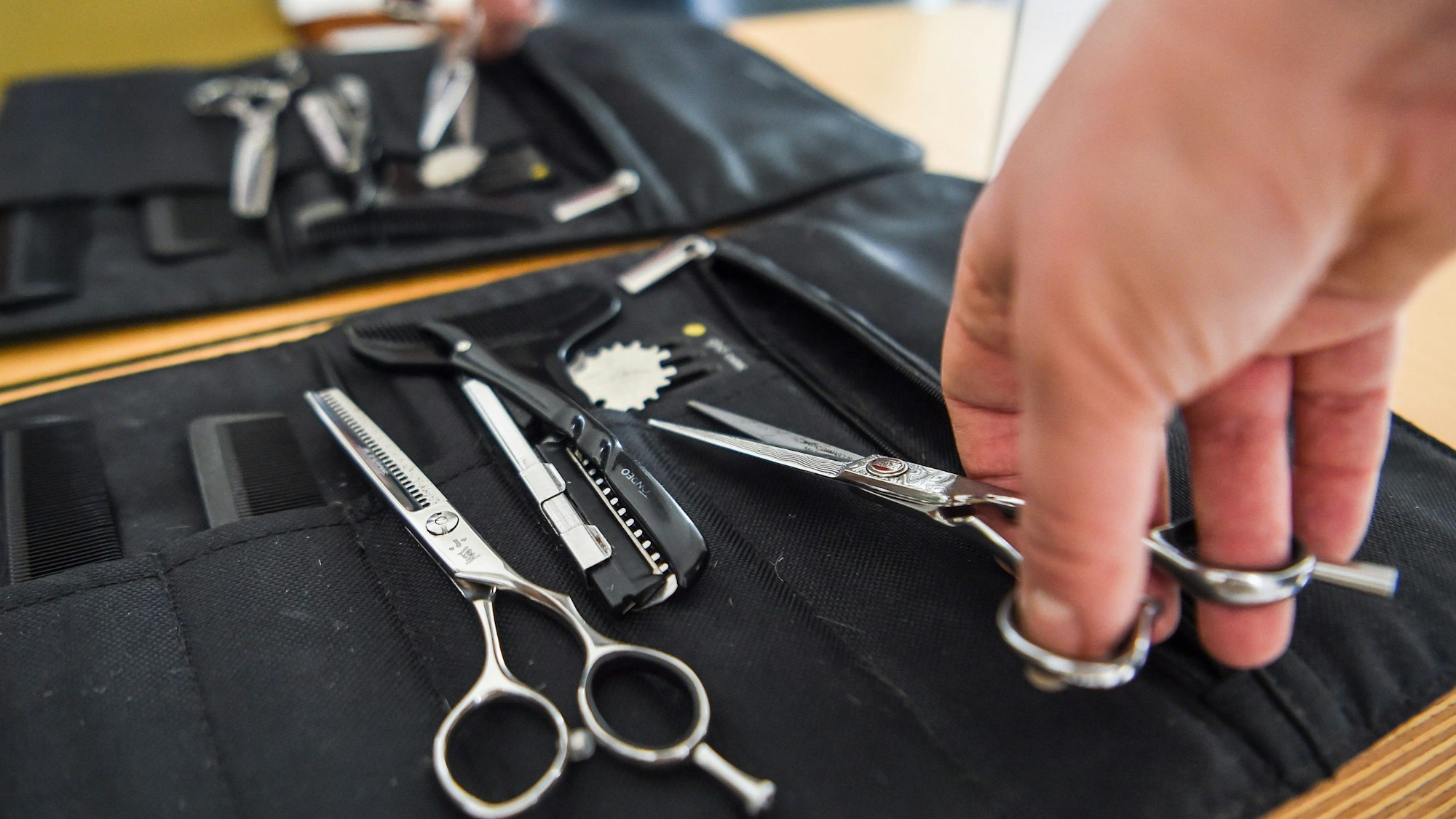 Eine Friseurin nimmt eine Haarschere aus ihrer Tasche. (Archivbild)