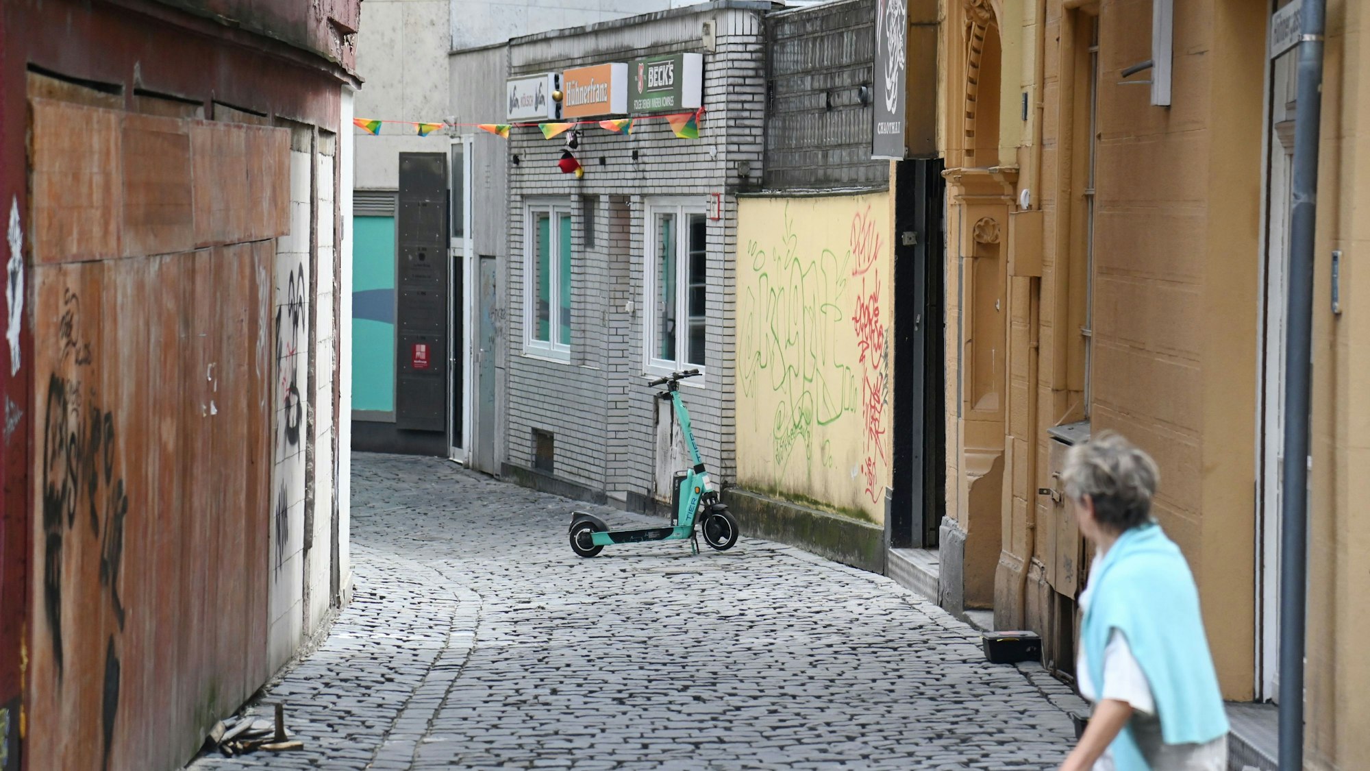 Eine Frau schaut in die Hühnergasse mit beschmierten und zugenagelten Häuserfassaden.