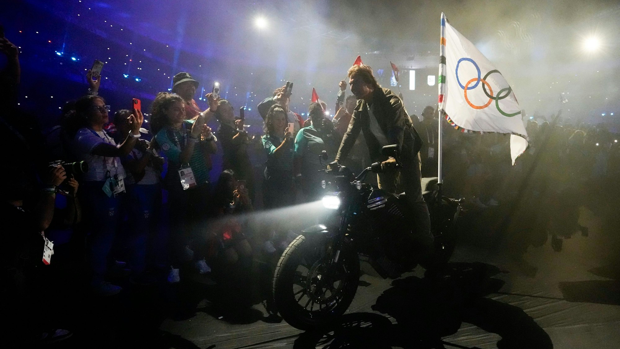 11.08.2024, Frankreich, Saint-Denis: Tom Cruise fährt auf einem Motorrad mit der olympischen Flagge während der Abschlussfeier der Olympischen Sommerspiele 2024 im Stade de France.