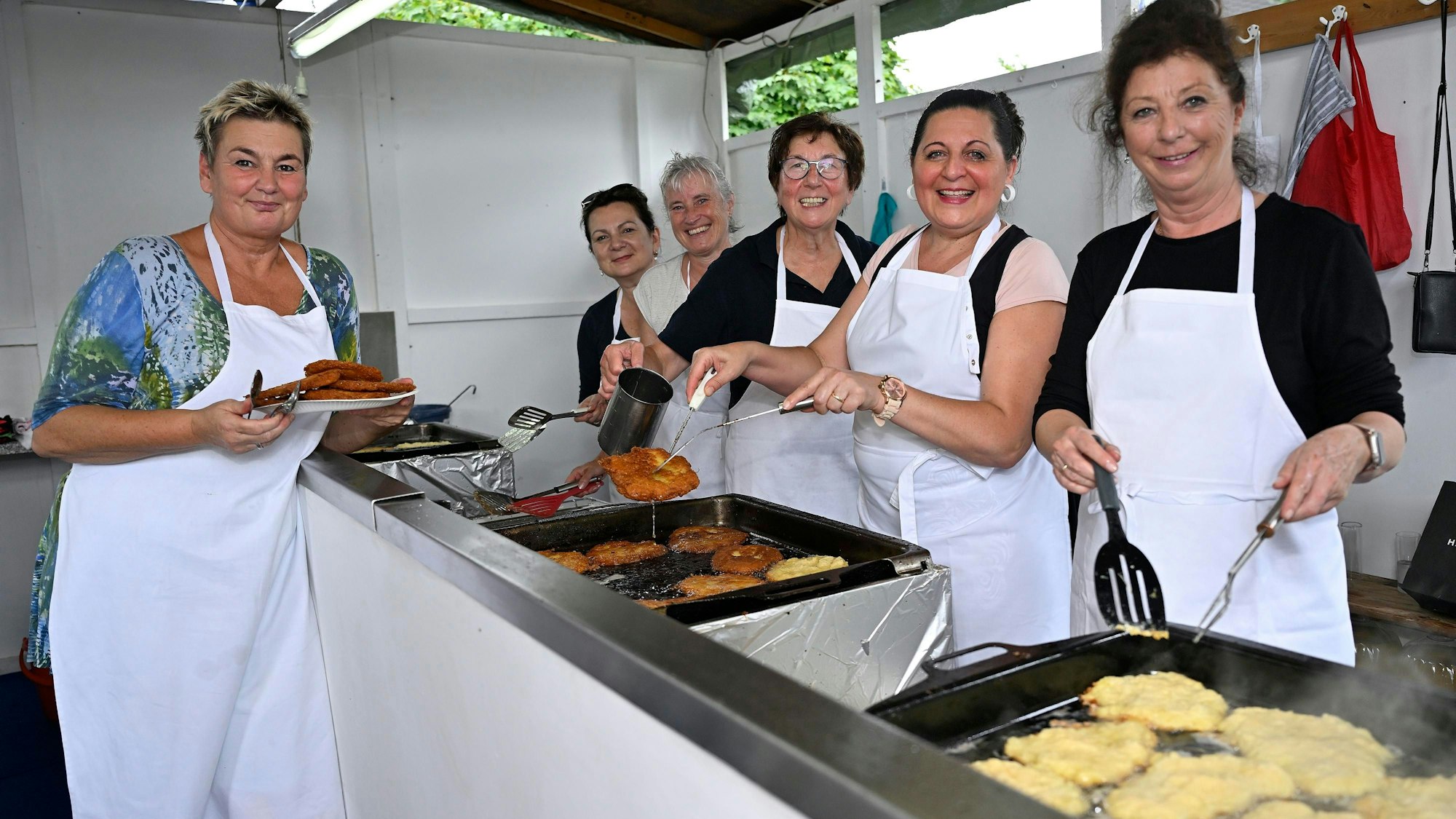 Sechs Köchinnen mit weißer Schürze stehen hinter den Pfannen und braten Reibekuchen.