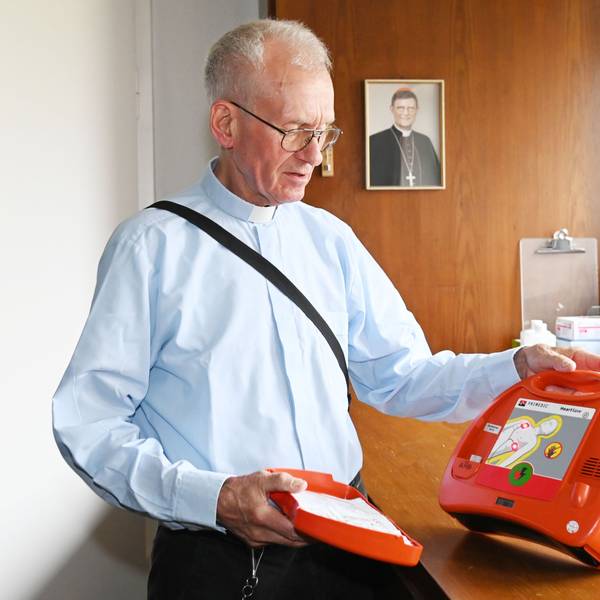 Pfarrer Franz Meurer zeigt einen Defibrillator in der Sakristei der Kirche Sankt Elisabeth in Köln. Im Hintergrund das Porträt des Kölner Erzbischofs, Kardinal Rainer Woelki