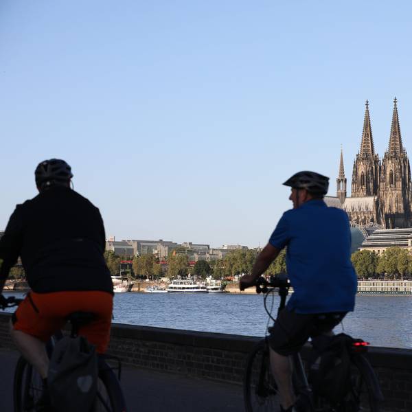 Radfahrer fahren am Rheinufer entlang, im Hintergrund ist der Kölner Dom zu sehen